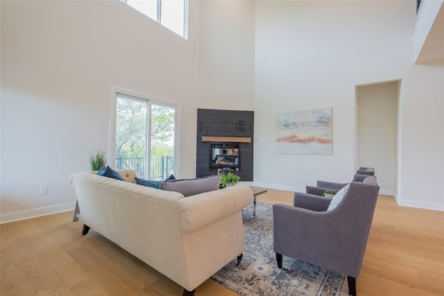 living room with light hardwood / wood-style floors, a towering ceiling, and a tiled fireplace