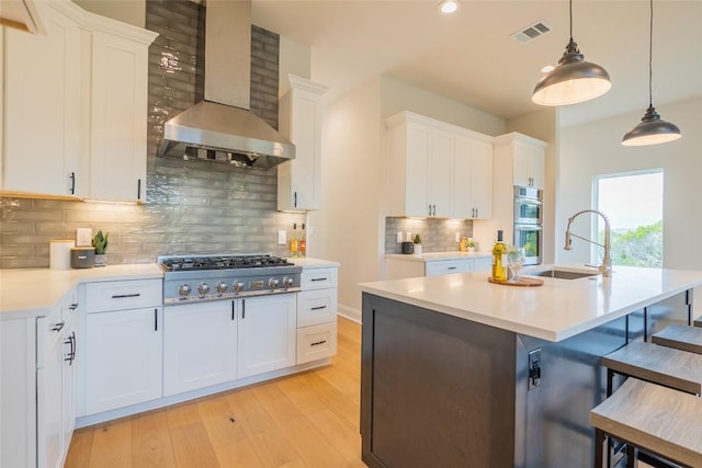 kitchen featuring white cabinets, wall chimney exhaust hood, appliances with stainless steel finishes, and tasteful backsplash