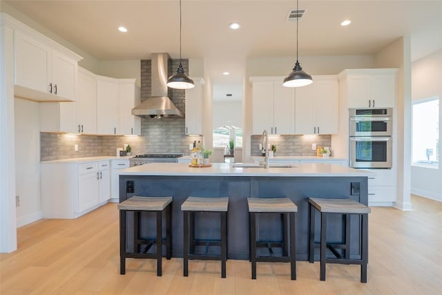 kitchen featuring wall chimney exhaust hood, stainless steel double oven, white cabinetry, and sink