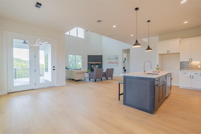 kitchen with backsplash, white cabinets, a center island with sink, sink, and hanging light fixtures