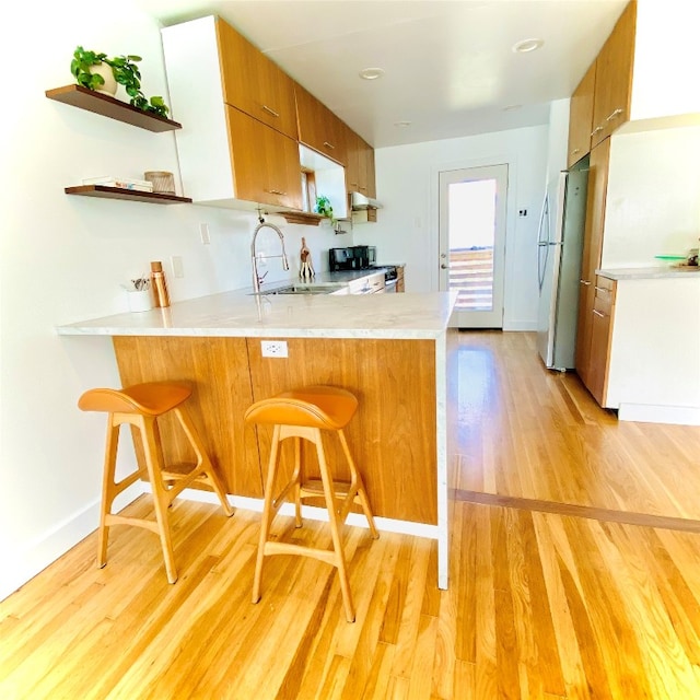 kitchen with kitchen peninsula, a kitchen breakfast bar, black range with gas cooktop, white refrigerator, and light hardwood / wood-style flooring