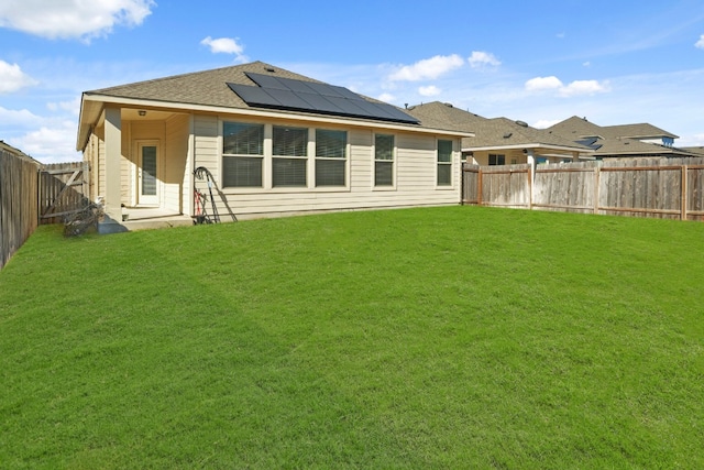 rear view of property featuring a lawn and solar panels