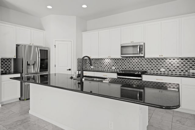 kitchen featuring appliances with stainless steel finishes, a center island with sink, white cabinetry, and dark stone countertops