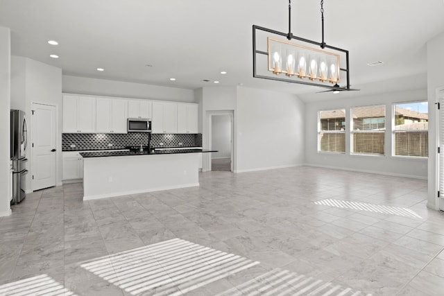 kitchen with appliances with stainless steel finishes, tasteful backsplash, decorative light fixtures, white cabinets, and an island with sink