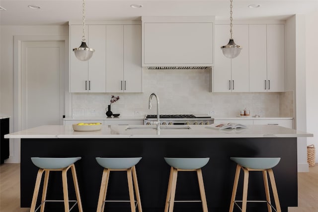 kitchen featuring light wood-type flooring, white cabinetry, a center island with sink, and decorative backsplash