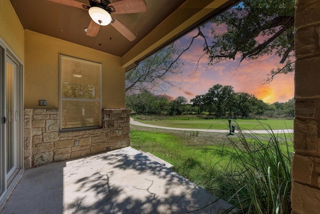 patio terrace at dusk with ceiling fan and a lawn