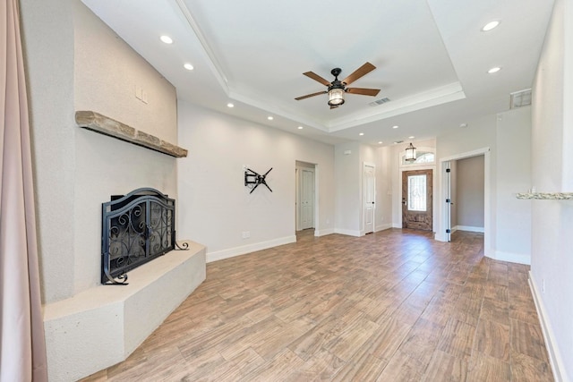 unfurnished living room with a raised ceiling, ceiling fan, and light hardwood / wood-style flooring