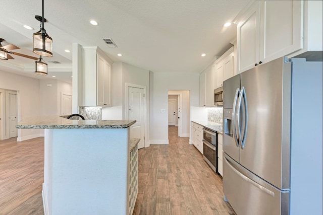 kitchen featuring pendant lighting, white cabinetry, appliances with stainless steel finishes, light wood-type flooring, and decorative backsplash