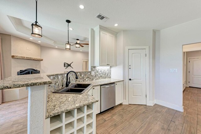 kitchen featuring pendant lighting, dishwasher, sink, kitchen peninsula, and light hardwood / wood-style flooring