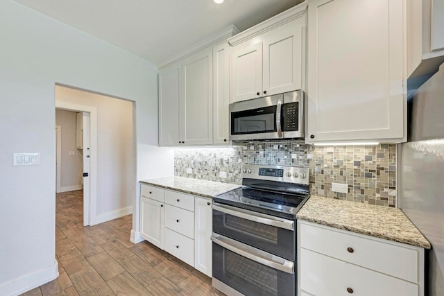 kitchen with light wood-type flooring, tasteful backsplash, white cabinetry, stainless steel appliances, and light stone countertops