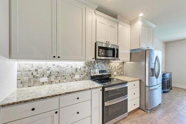 kitchen featuring appliances with stainless steel finishes, white cabinets, backsplash, light stone countertops, and light wood-type flooring