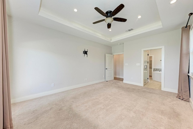 unfurnished bedroom featuring ceiling fan, a raised ceiling, ornamental molding, light colored carpet, and ensuite bathroom