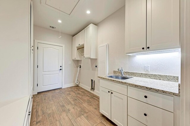 kitchen with light hardwood / wood-style floors, light stone countertops, sink, and white cabinets