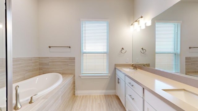 bathroom featuring a relaxing tiled tub, vanity, a healthy amount of sunlight, and hardwood / wood-style floors