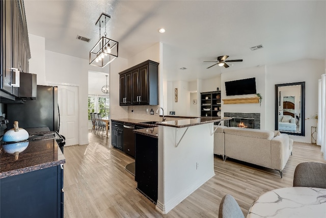 kitchen with ceiling fan with notable chandelier, pendant lighting, a kitchen bar, light hardwood / wood-style flooring, and dark brown cabinetry