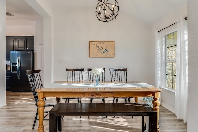 dining space with light wood-type flooring, vaulted ceiling, and a chandelier