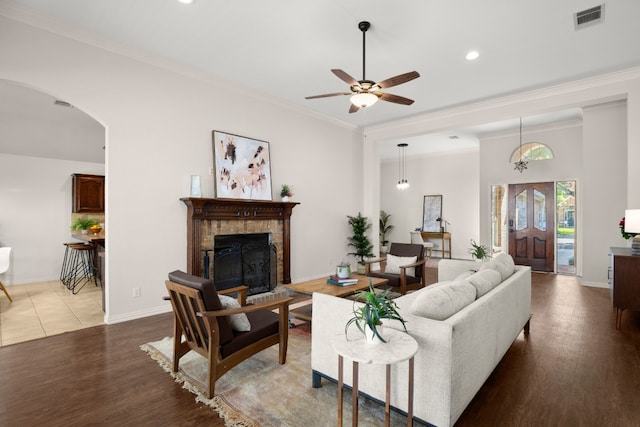 living room featuring wood-type flooring, a brick fireplace, crown molding, and ceiling fan