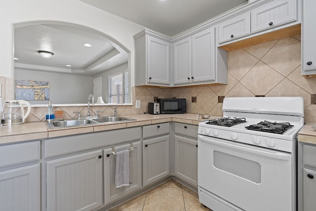 kitchen with light tile patterned flooring, sink, tile counters, white gas range oven, and decorative backsplash