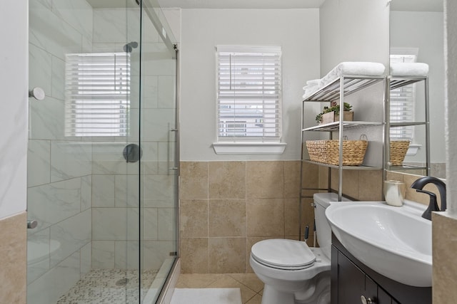 bathroom with a shower with shower door, tile walls, tile patterned flooring, vanity, and toilet