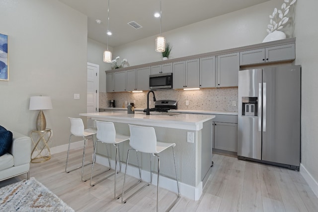 kitchen with gray cabinetry, decorative backsplash, stainless steel appliances, and a center island with sink