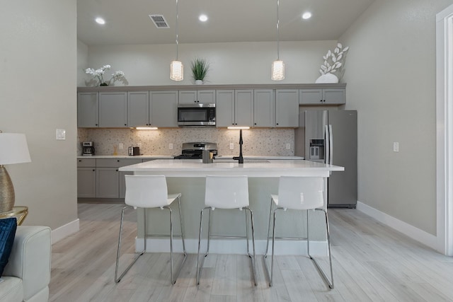 kitchen with a breakfast bar, hanging light fixtures, a center island with sink, gray cabinets, and stainless steel appliances