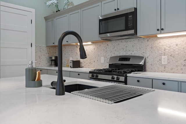 kitchen with sink, gray cabinets, stainless steel appliances, tasteful backsplash, and light stone counters