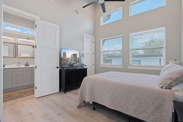 bedroom with a towering ceiling, sink, ceiling fan, and light hardwood / wood-style flooring