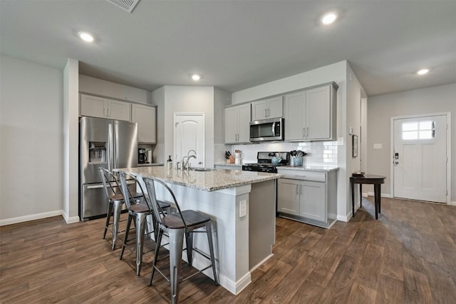 kitchen featuring appliances with stainless steel finishes, an island with sink, light stone countertops, gray cabinets, and dark hardwood / wood-style floors