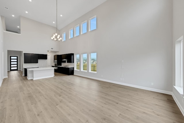 unfurnished living room featuring an inviting chandelier, light hardwood / wood-style flooring, and a high ceiling