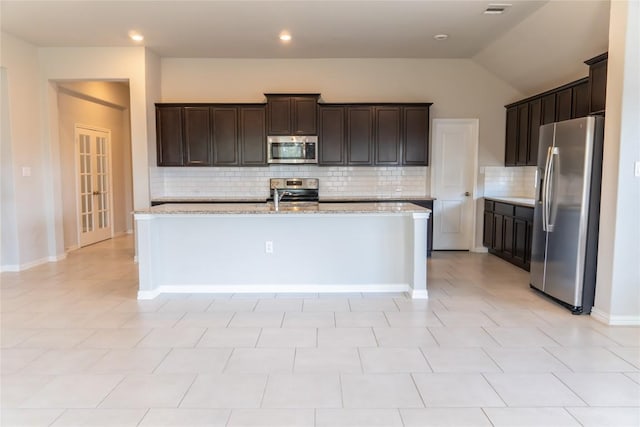 kitchen featuring light stone counters, lofted ceiling, appliances with stainless steel finishes, and tasteful backsplash