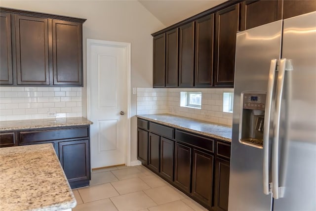 kitchen featuring light stone countertops, tasteful backsplash, vaulted ceiling, stainless steel fridge with ice dispenser, and light tile patterned flooring