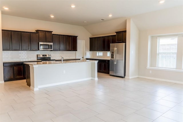 kitchen with a kitchen island with sink, vaulted ceiling, decorative backsplash, light stone counters, and stainless steel appliances