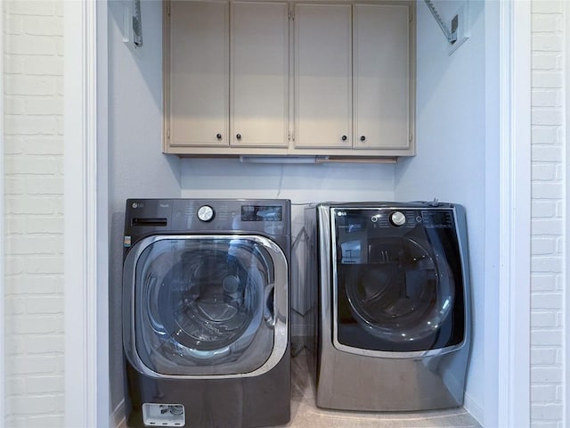 washroom with brick wall, independent washer and dryer, and cabinets