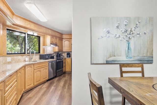 kitchen with light stone countertops, sink, backsplash, wood-type flooring, and appliances with stainless steel finishes