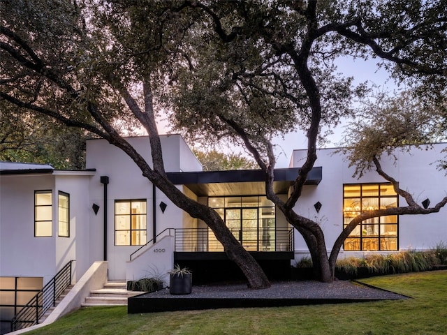 back house at dusk featuring a lawn