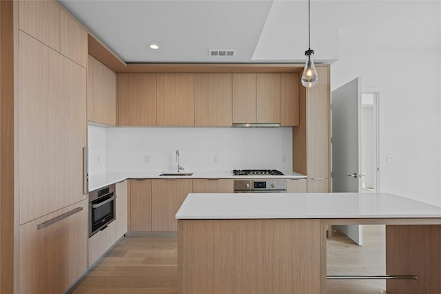 kitchen featuring light brown cabinetry, decorative light fixtures, appliances with stainless steel finishes, and light wood-type flooring