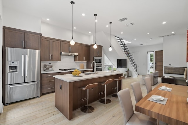 kitchen with a center island with sink, sink, hanging light fixtures, dark brown cabinetry, and stainless steel appliances