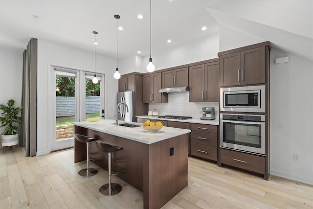 kitchen with sink, stainless steel appliances, an island with sink, decorative light fixtures, and dark brown cabinets