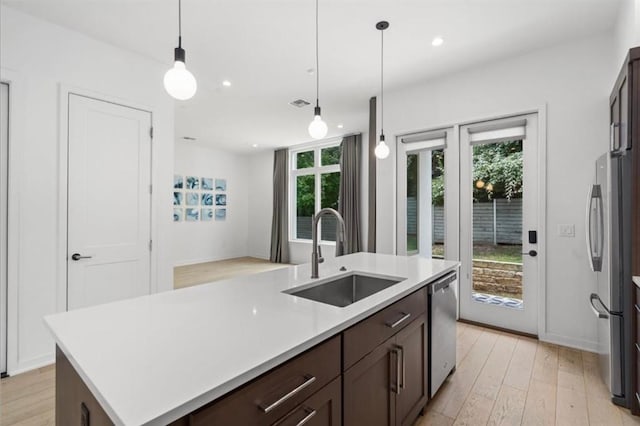 kitchen featuring a center island with sink, hanging light fixtures, stainless steel appliances, light countertops, and a sink