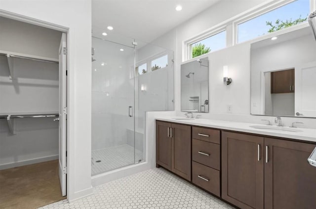 full bathroom with double vanity, a shower stall, a walk in closet, and a sink