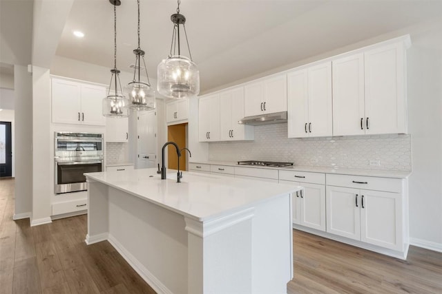 kitchen featuring stainless steel appliances, sink, pendant lighting, a center island with sink, and white cabinets