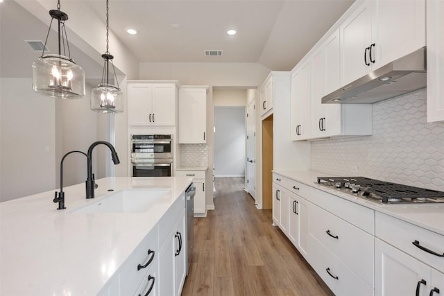 kitchen with stainless steel appliances, sink, pendant lighting, white cabinets, and light hardwood / wood-style floors