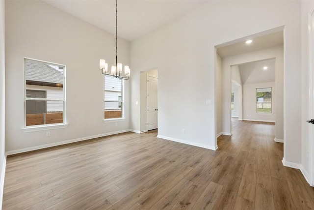 unfurnished dining area featuring hardwood / wood-style floors, high vaulted ceiling, and a notable chandelier