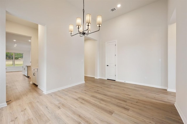 unfurnished dining area with a high ceiling, light hardwood / wood-style flooring, and an inviting chandelier