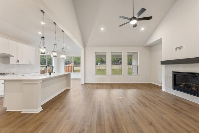 kitchen with ceiling fan, a center island with sink, white cabinetry, hanging light fixtures, and a tiled fireplace