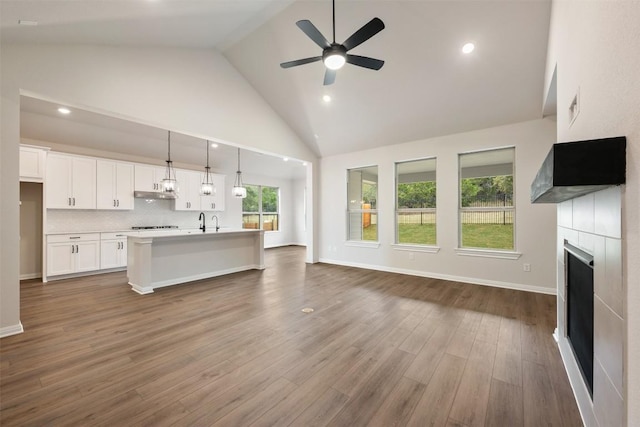 unfurnished living room featuring ceiling fan, sink, wood-type flooring, high vaulted ceiling, and a tiled fireplace