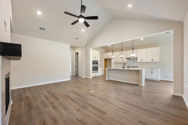 unfurnished living room with light wood-type flooring, high vaulted ceiling, and ceiling fan