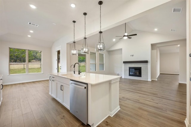 kitchen featuring a kitchen island with sink, a tile fireplace, sink, light hardwood / wood-style flooring, and stainless steel dishwasher