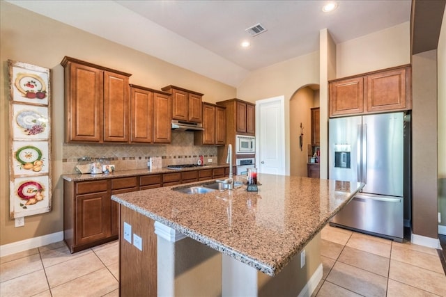 kitchen featuring appliances with stainless steel finishes, a center island with sink, vaulted ceiling, and light stone counters