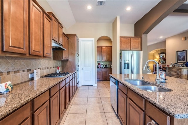 kitchen with light stone countertops, sink, stainless steel appliances, a center island with sink, and light tile patterned floors